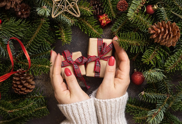 Female hands holding two gift boxes on a wooden table near Christmas decorations top view