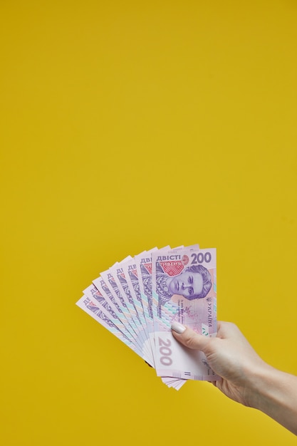 Female hands holding Ukrainian banknotes on yellow