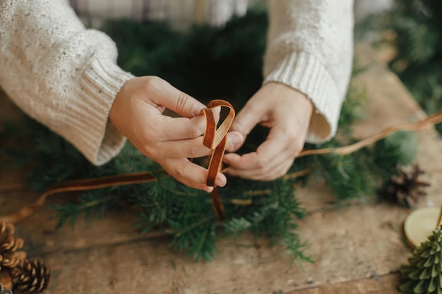 ベルベットのリボンを保持し、素朴な木製のテーブルでクリスマス リースを飾る女性の手