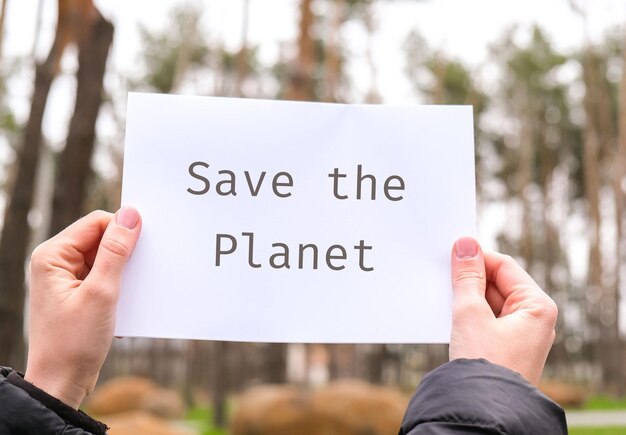 Photo female hands holding white paper sheet with text save the planet outdoors nature background