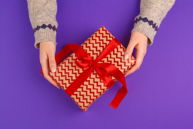 Female hands holding wrapped gift on purple background