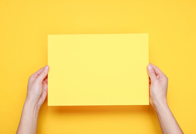 Female hands holding yellow paper sheet on yellow