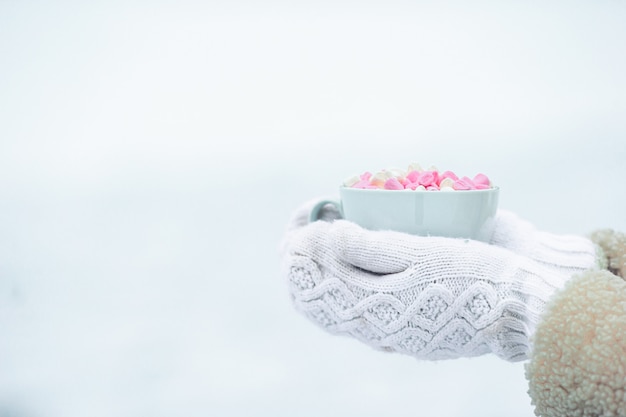 Female hands holdink white cup of coffee with white and pink marshmallows