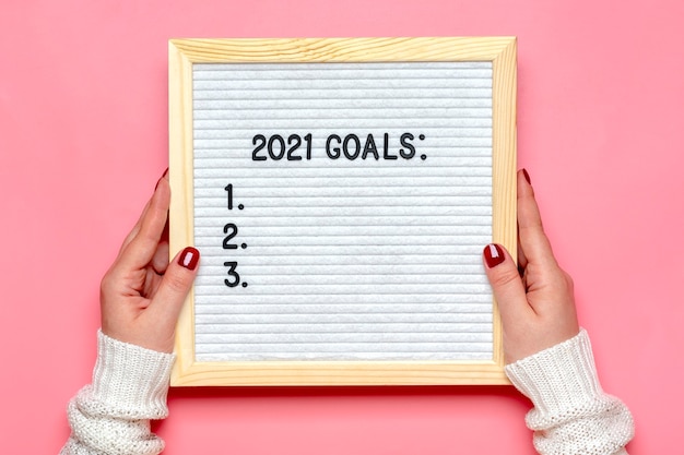 Female hands holds felt board with text - 2021 goals on pink