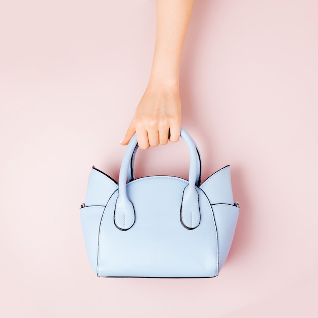 Photo female hands holds handbag on pink  background . flat lay, top view. spring fashion concept in pastel colored