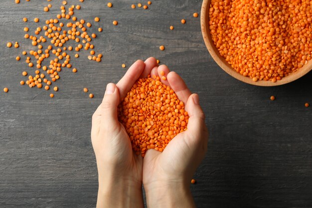 Female hands holds red legumes over a dark surface with bowl of legumes