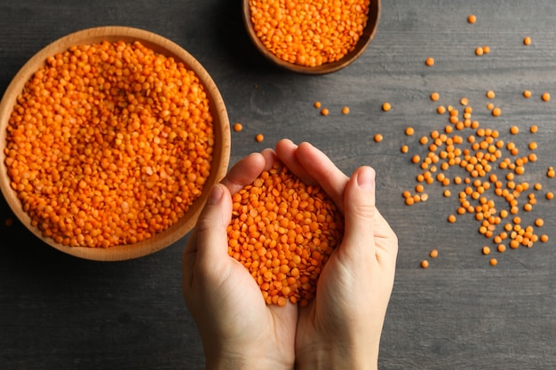 Female hands holds red legumes over a dark with bowls of legumes