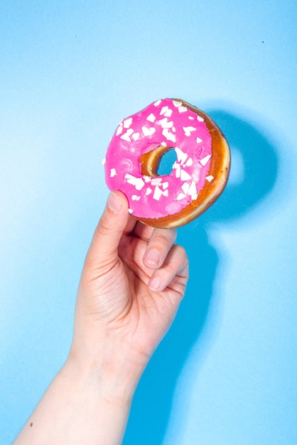 Le mani femminili tengono le ciambelle glassate con zucchero dolce su sfondo blu