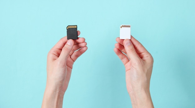 Female hands holds two SD memory cards on blue. Minimalist Techno Concept.