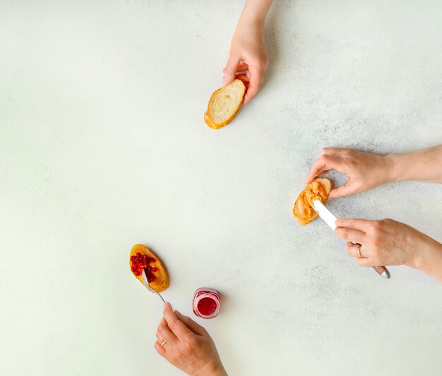 Female hands illustrating stages of making peanut butter and jelly sandwich, top view, copy space