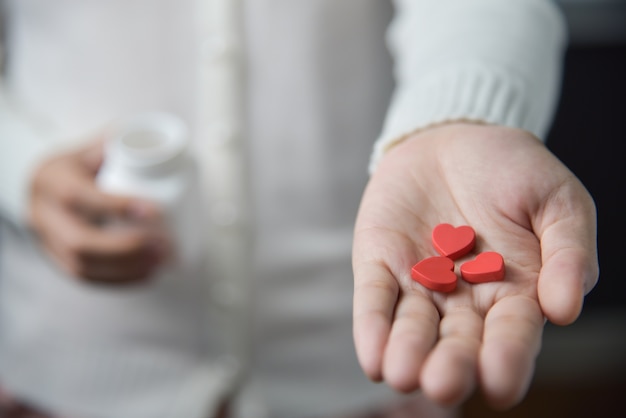 Foto le mani femminili sta tenendo le pillole rosse nella forma del cuore