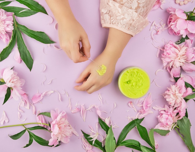 Female hands and a jar with thick green scrub and pink flowering peonies