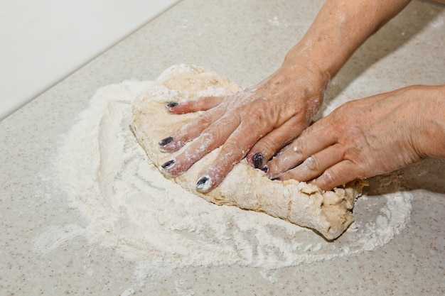 Foto le mani femminili impastano l'impasto con la farina su un tavolo bianco di cucina vista superiore preparazione della cottura fase di cottura