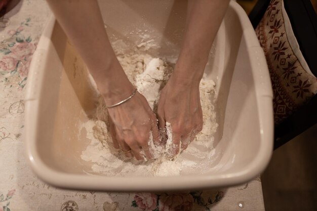 Female hands kneading dough in bowl on table close up