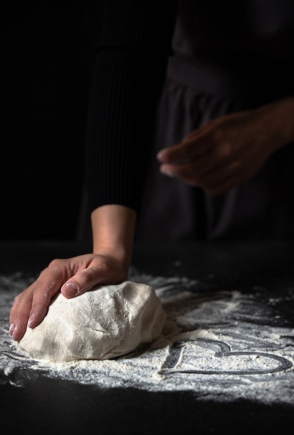 Female hands kneading fresh dough on a black table