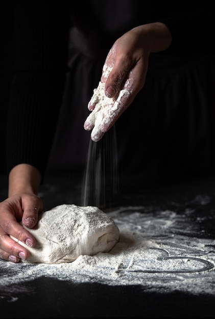 Female hands kneading fresh dough on a black table