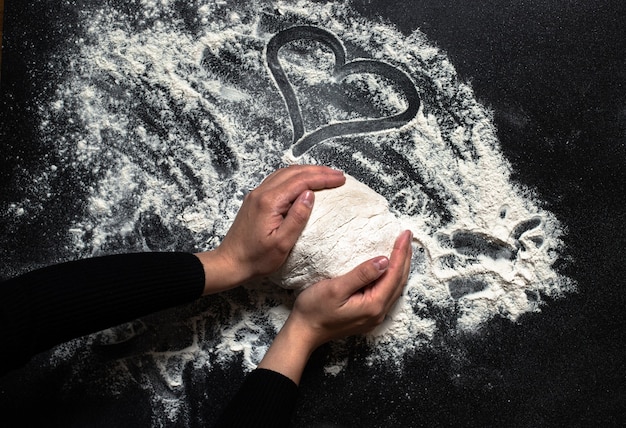 Female hands kneading fresh dough on a black table