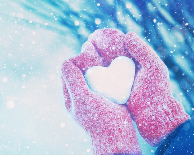 Female hands in knitted mittens with heart of ice in winter day. Love concept.