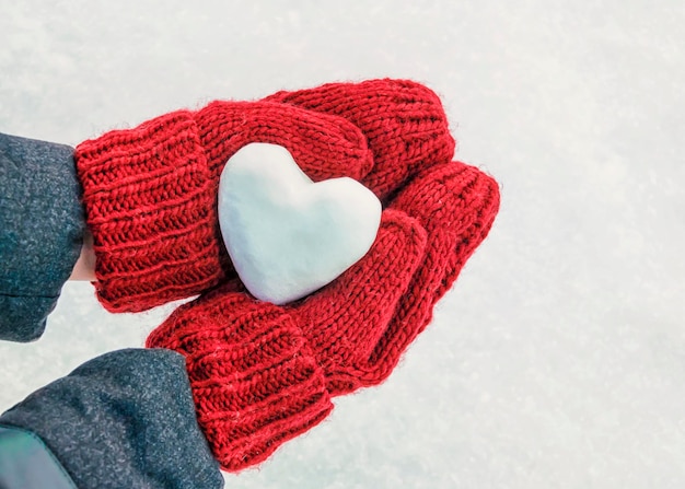 Female hands in knitted mittens with heart of snow in winter day