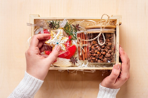 Female hands laid care package, seasonal gift box with coffee, gingerbread and cinnamon