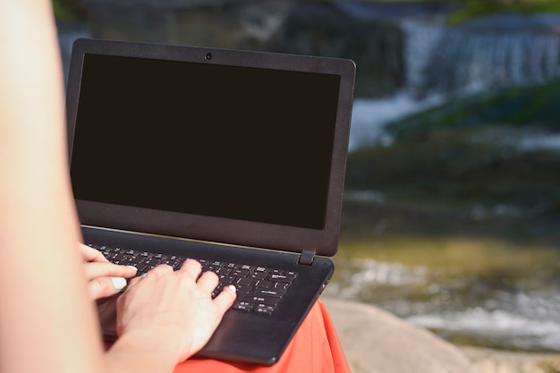 Foto mani e computer portatile femminili contro lo sfondo del fiume