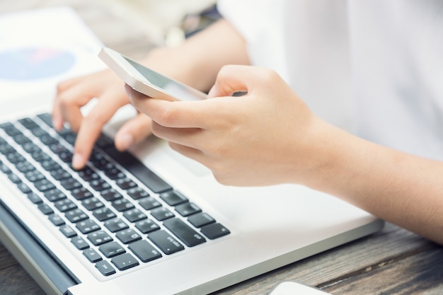 Female hands on laptop keyboard and holding smart phone