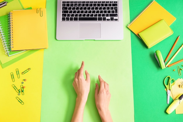 Female hands, laptop and stationery, top view