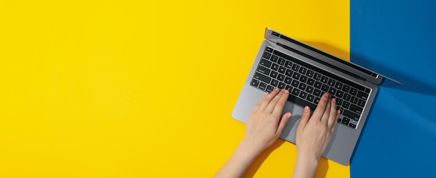 Female hands and laptop on yellow blue background