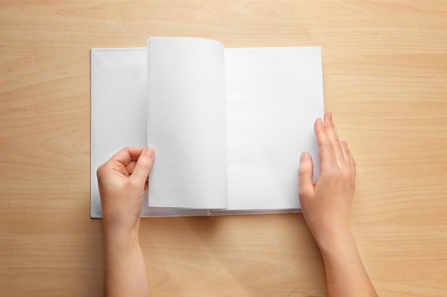 female hands leafing through book with blank pages on wooden background