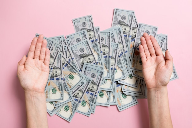 Female hands lying on stack of one hundred dollar bills on colorful background