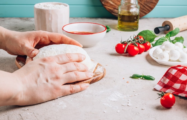 Foto mani femminili fanno la pizza gli ingredienti per la pizza margherita fatta in casa sulla superficie di pietra