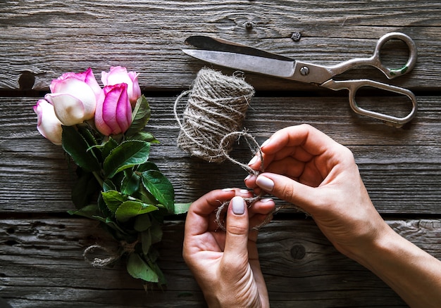 バラと木製のテーブルに花束を作る女性の手。フラワーズ