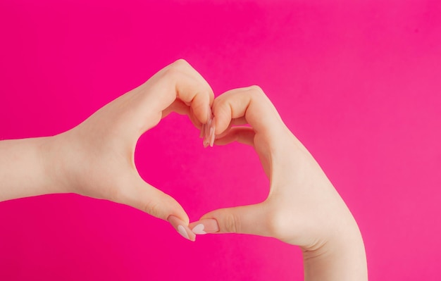 Женские руки делают жест сердца на розовом фоне