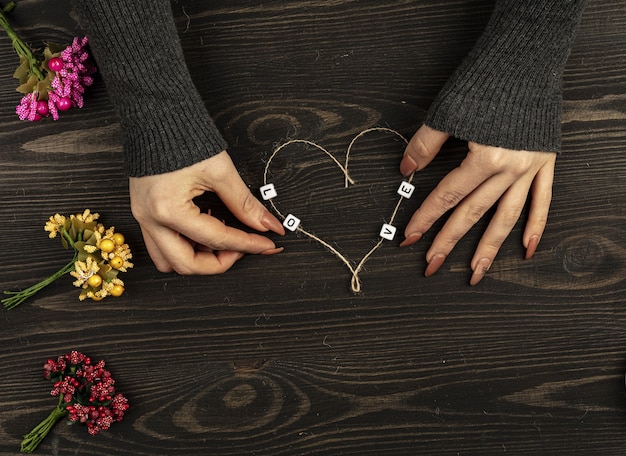 Female hands making heart shape from thread on wooden table.