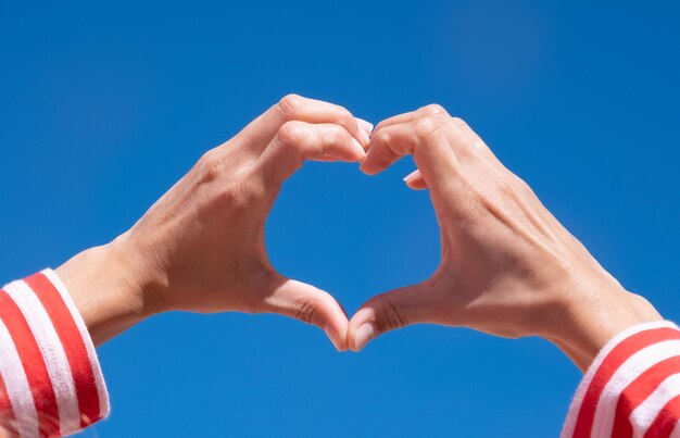 Female hands making sign heart by fingers on sky background