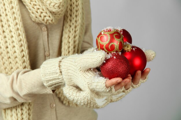 Mani femminili in guanti sfere dell'albero di natale, sulla superficie del colore