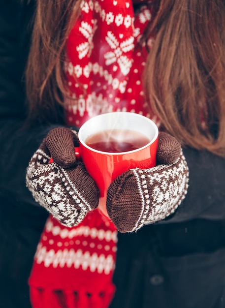 Female hands in mittens holding a cup of tea