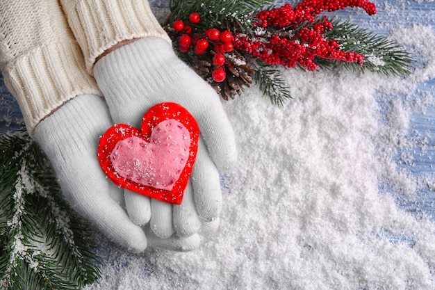 Female hands in mittens with decorative heart on snow background