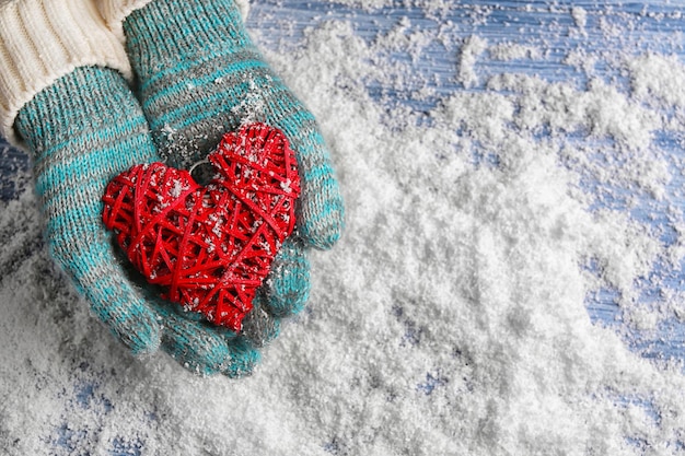 Female hands in mittens with decorative heart on snow background