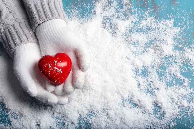 Female hands in mittens with decorative heart on snow background