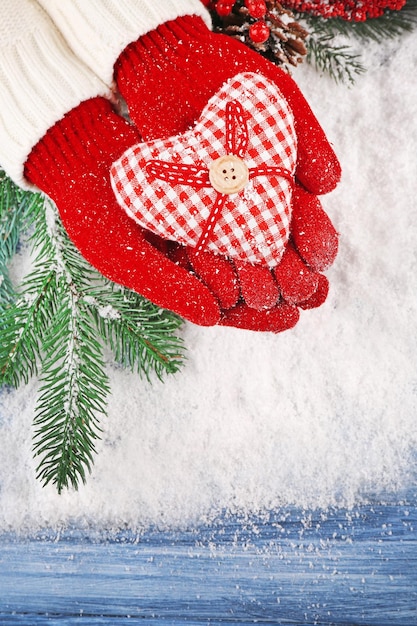 Женские руки в рукавицах с декоративным сердцем на фоне снега