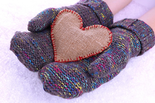 Photo female hands in mittens with heart on snow background