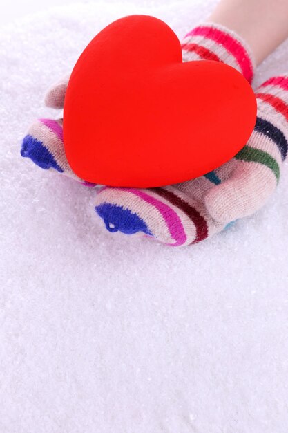 Mani femminili in guanti con cuore su sfondo di neve