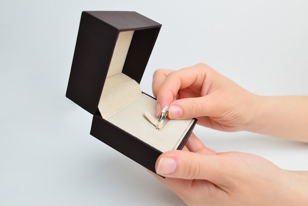 Female hands open a box with a diamond ring on a white\
background