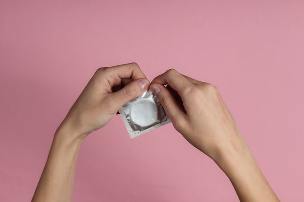 Женские руки открывают презерватив на розовой бумаге