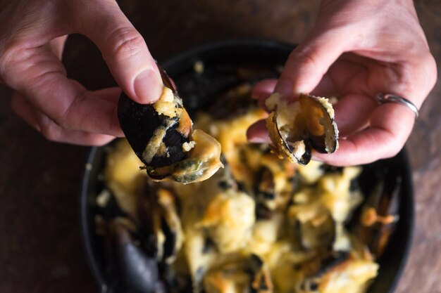 Female hands open the doors of mussels with cheese sauce