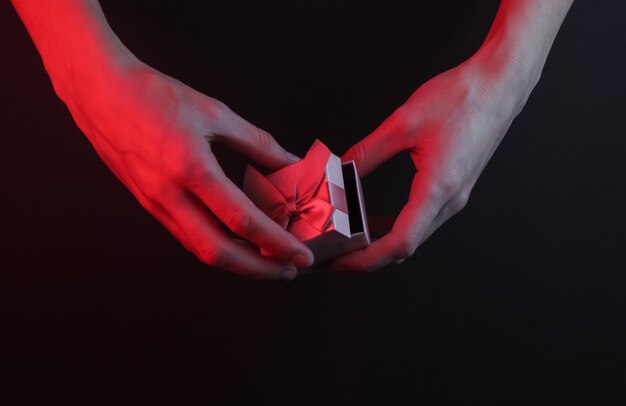 Mani femminili aprono una confezione regalo con un fiocco su uno sfondo nero con luce al neon rossa