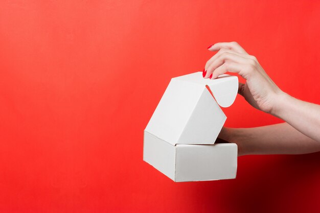 Female hands open white box on red background