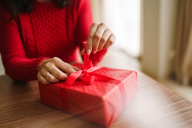 Mani femminili che aprono la confezione regalo rossa disimballaggio di un regalo concetto di celebrazione del giorno di san valentino