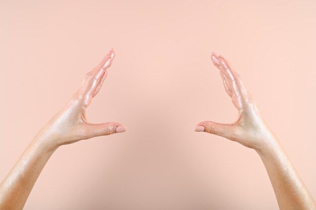 Female hands painted in silver holding something over pink wall High quality photo